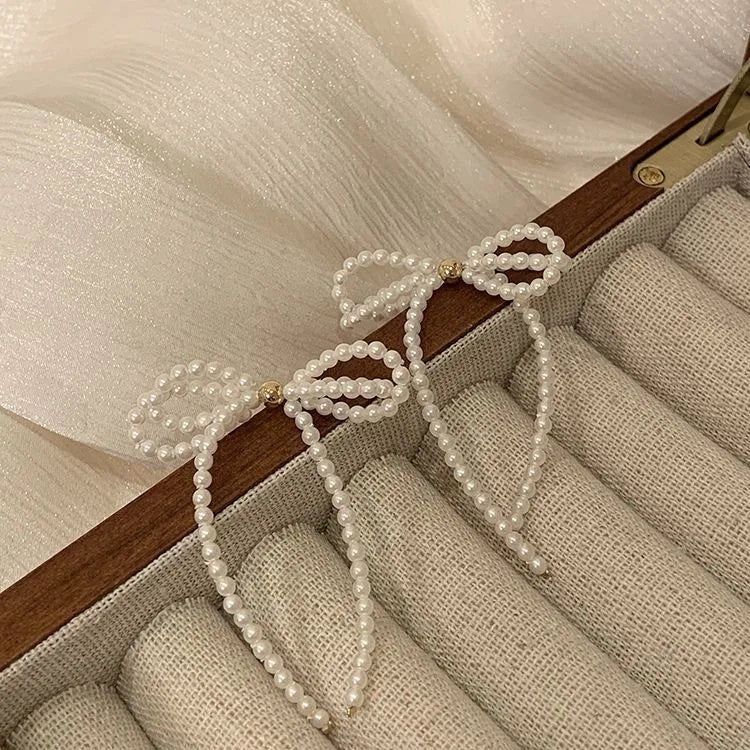 Delicate handcrafted earrings featuring white seed bead bow design and long dangle detail