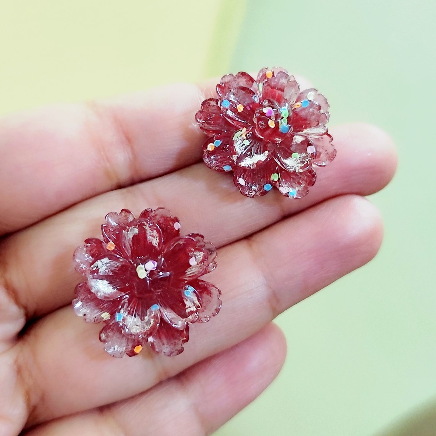 Pink floral earrings held between fingers with a blurred green background