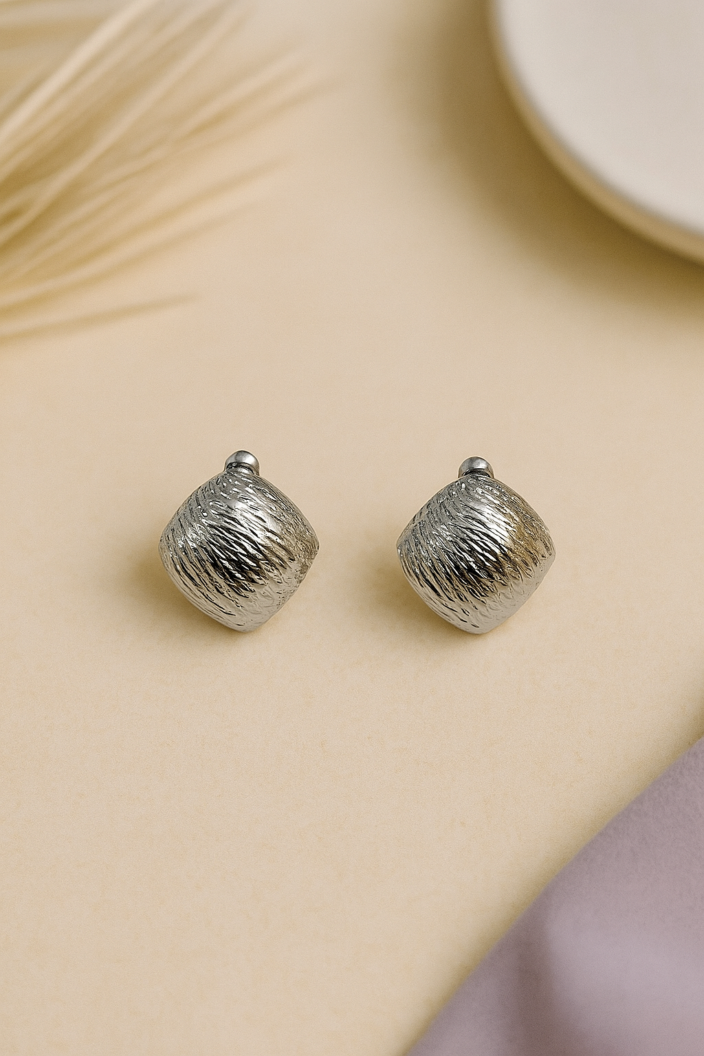 Silver textured earrings on a beige surface