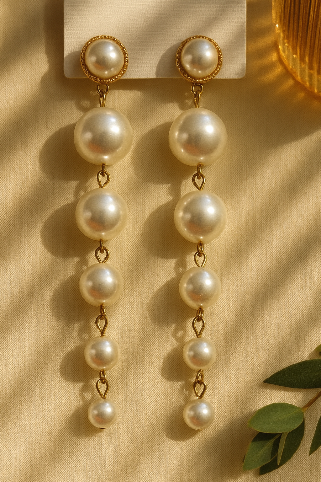 Gold drop earrings with graduated white pearls on a beige fabric background