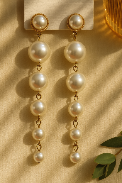 Gold drop earrings with graduated white pearls on a beige fabric background