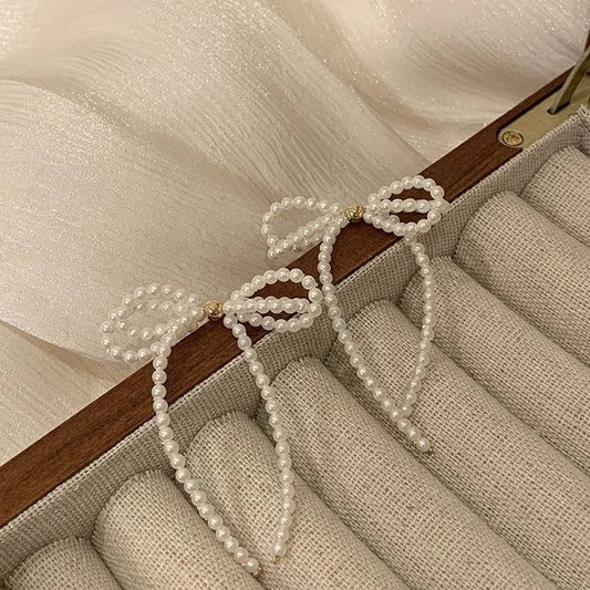 Delicate handcrafted earrings featuring white seed bead bow design and long dangle detail