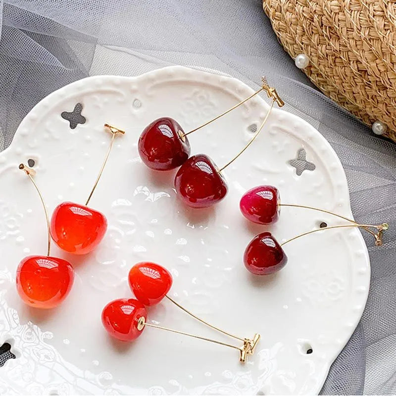 Cherry-shaped jewelry pins on a decorative plate with a woven basket in the background.