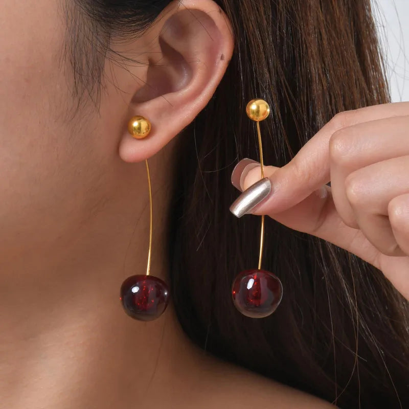 Gold and red earrings being worn and held by a person