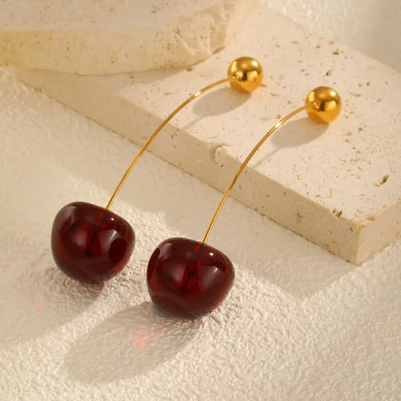 Cherry-shaped earrings with gold hooks on a textured beige surface